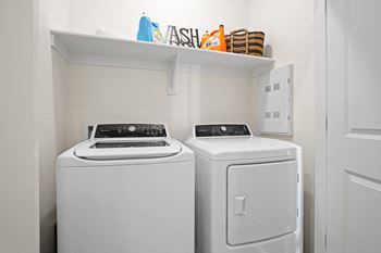 A white washer and dryer in a white laundry room with a shelf above